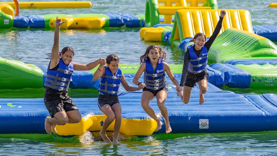 Children in life vests playing on colorful inflatable water park obstacles in ocean