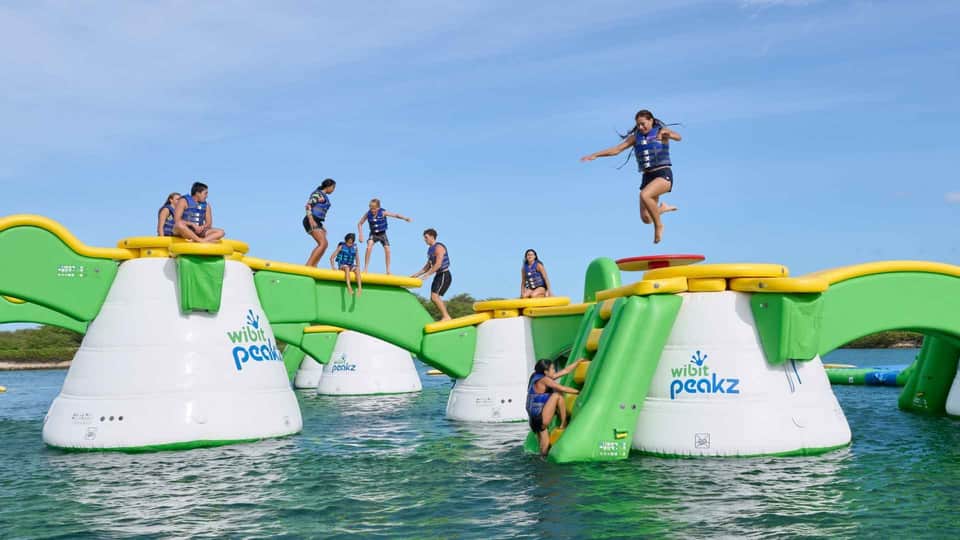Inflatable water playground obstacle course with children jumping and climbing in turquoise water