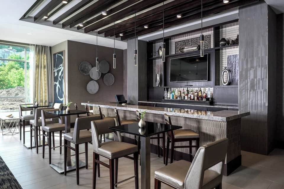 Contemporary hotel bar with dark wood cabinetry, pendant lighting, flat-screen TV, and bar seating