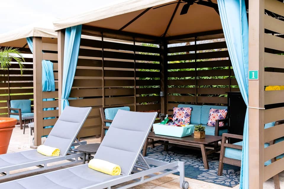 Covered outdoor lounge area with loungers, blue cushions, curtains, and modern shade structures