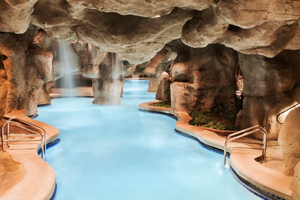 Spa indoor grotto pool with natural stone cave ceiling, waterfall feature, and thermal water