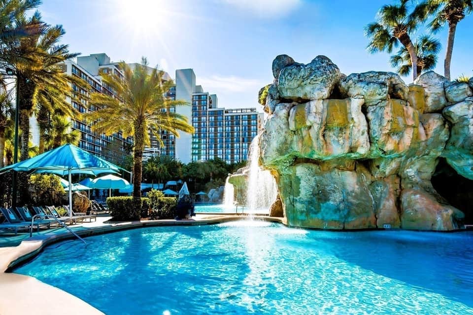 Resort pool with turquoise water, rock waterfall feature, and downtown hotel towers