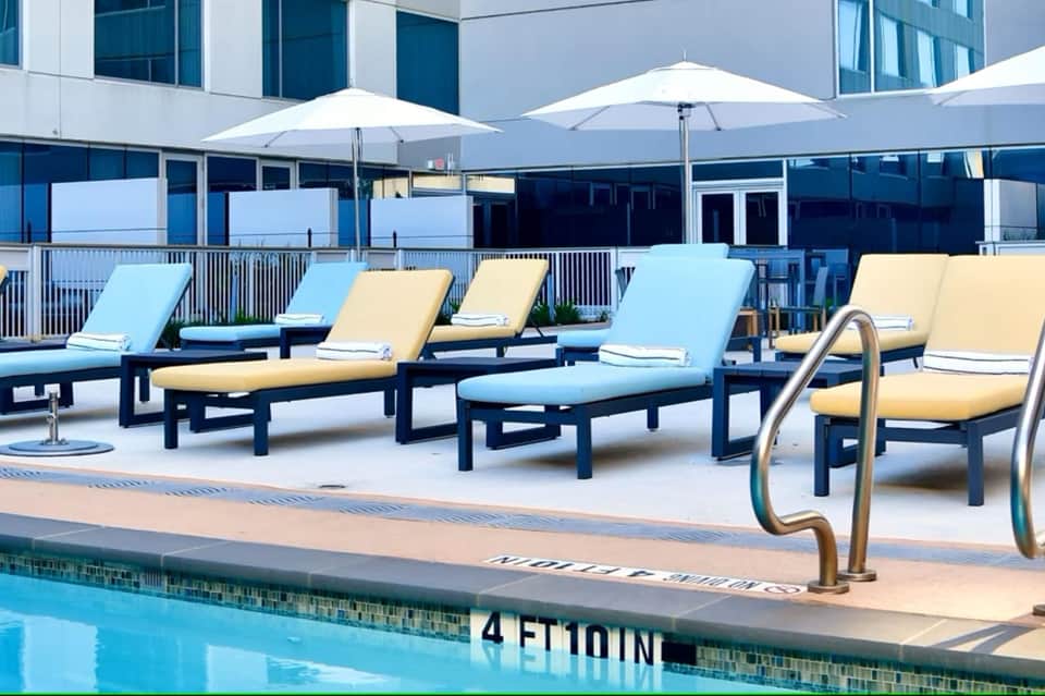 Modern rooftop pool deck with lounge chairs in blue and yellow cushions under white umbrellas