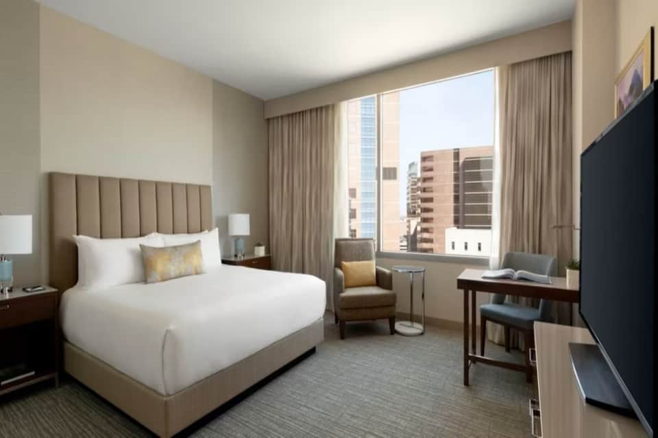 Modern hotel room with beige headboard, city skyline view, and contemporary furnishings