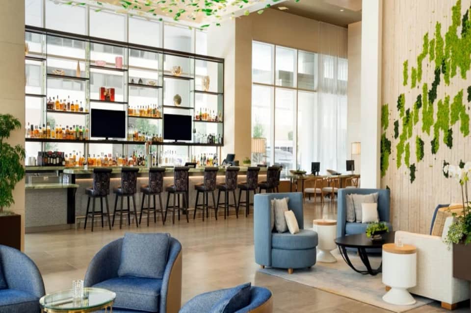 Modern hotel lobby bar with living green wall, blue seating, and well-stocked shelving