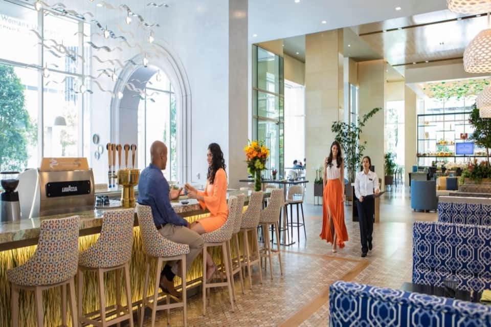 Modern hotel lobby with coffee counter, high ceilings, plants, and contemporary seating