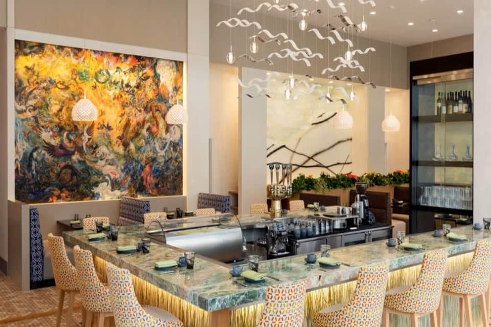 Upscale restaurant bar with abstract artwork, artistic lighting fixture, and marble-topped counter seating