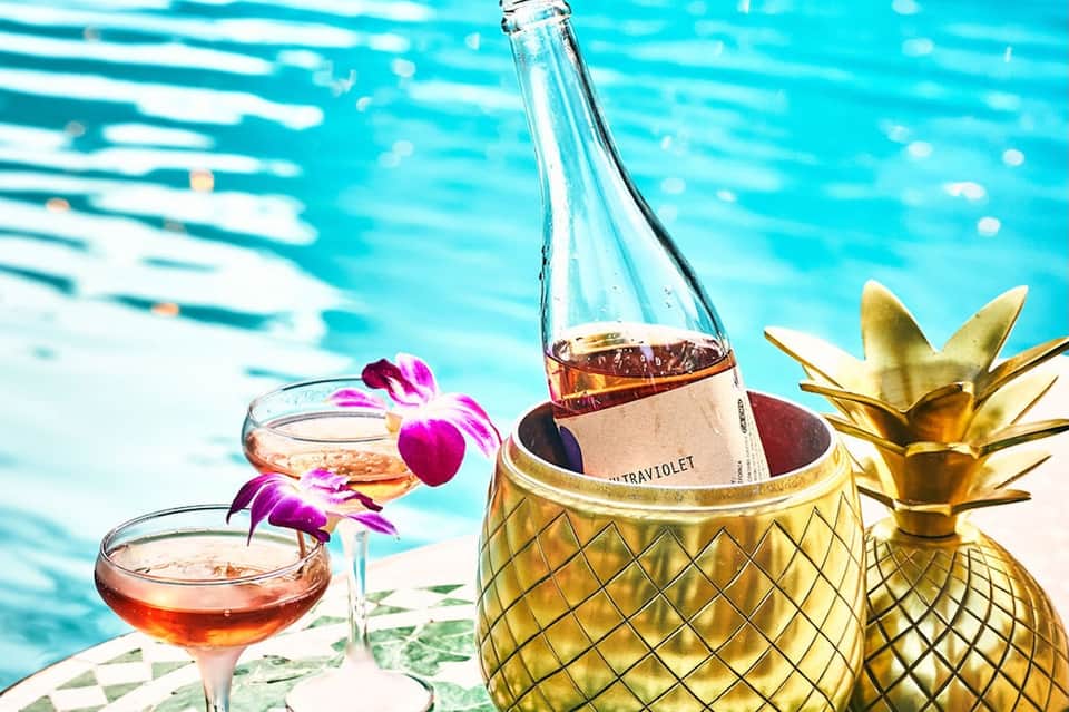 Cocktails and rosé wine by pool with orchids and golden pineapple ice bucket