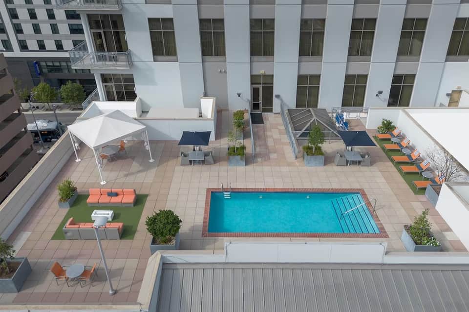 Rooftop pool deck with turquoise pool, lounge chairs, white tent, and urban courtyard view