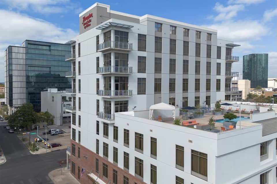 Modern white hotel building exterior with pool deck and rooftop amenities area visible