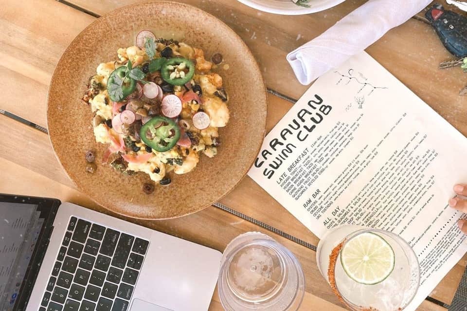 Colorful scrambled egg dish with jalapeños and radishes on cork plate, laptop and menu visible
