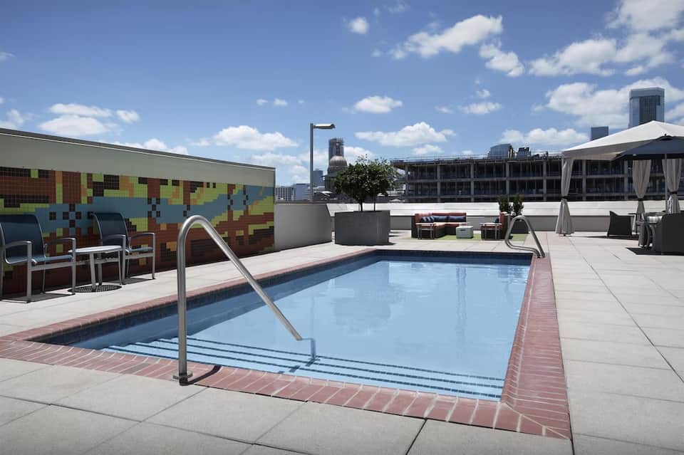 Rooftop pool deck with blue swimming pool, colorful mosaic art wall, and urban city skyline views