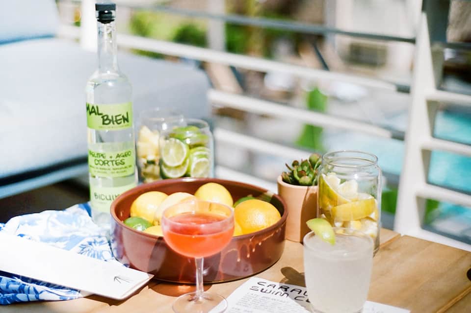 Poolside table setup with mezcal bottle, citrus cocktails, and fresh lemons
