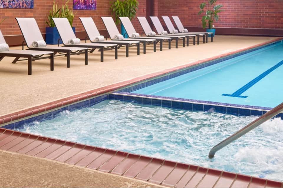 Indoor pool area with lap pool, hot tub, loungers with striped cushions, and brick walls