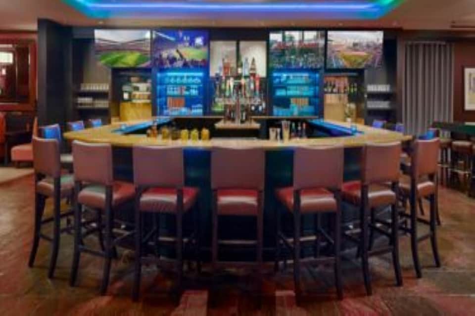 Modern bar lounge with curved counter, blue accent lighting, and multiple display screens