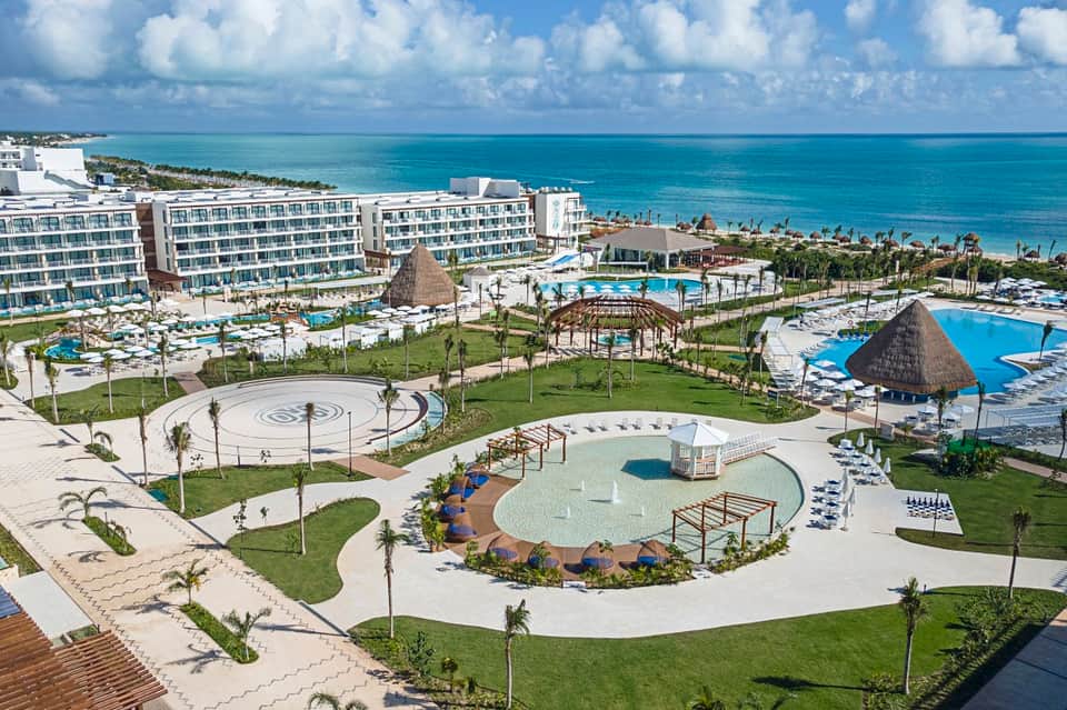 All-inclusive beachfront resort aerial view with multiple pools, thatched umbrellas, hotel buildings, and Caribbean sea