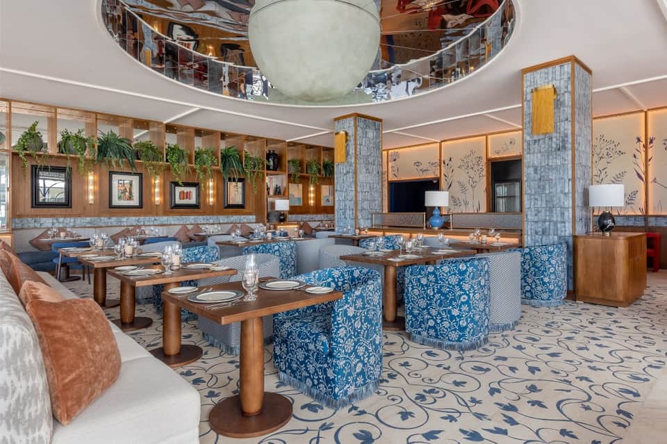 Modern upscale restaurant with blue patterned chairs, wooden tables, and architectural ceiling detail