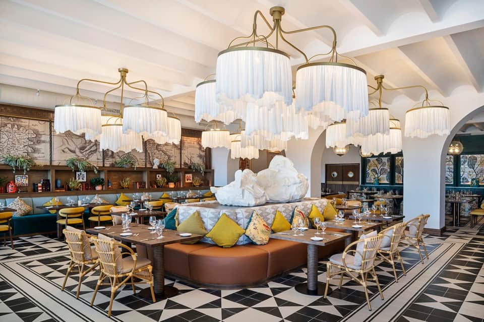 Upscale hotel restaurant with ornate chandeliers, bold yellow and blue cushions, and marble flooring
