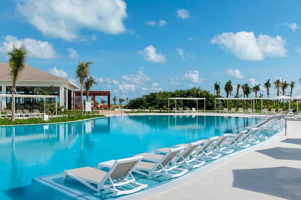 Rectangular resort pool with white loungers, cabanas, and manicured landscape