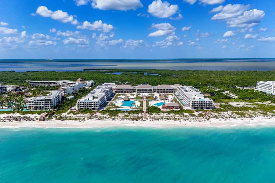 Aerial view of beachfront resort complex with pools, buildings, pristine beach, and turquoise water