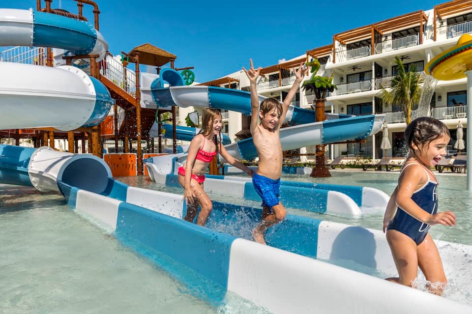 Family fun pool area with colorful water slides, shallow children's pools, and multi-story resort buildings