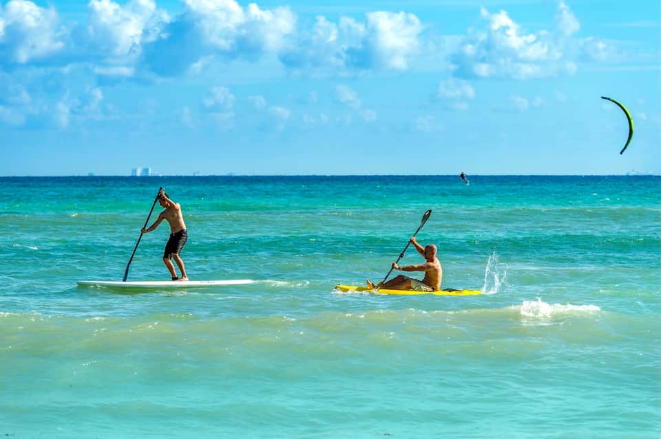 Beachgoers paddle boarding and kiteboarding in turquoise tropical ocean waters
