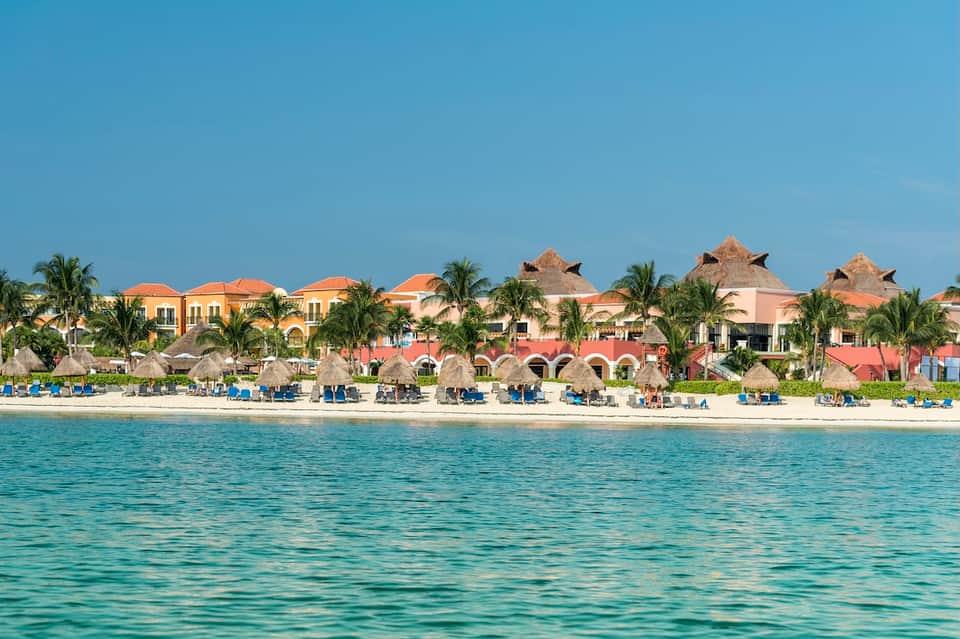Beachfront luxury resort with thatched cabanas, palm trees, and pristine turquoise ocean water