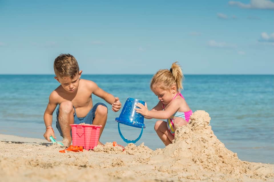 Children building sandcastle on beach with ocean and blue sky in background