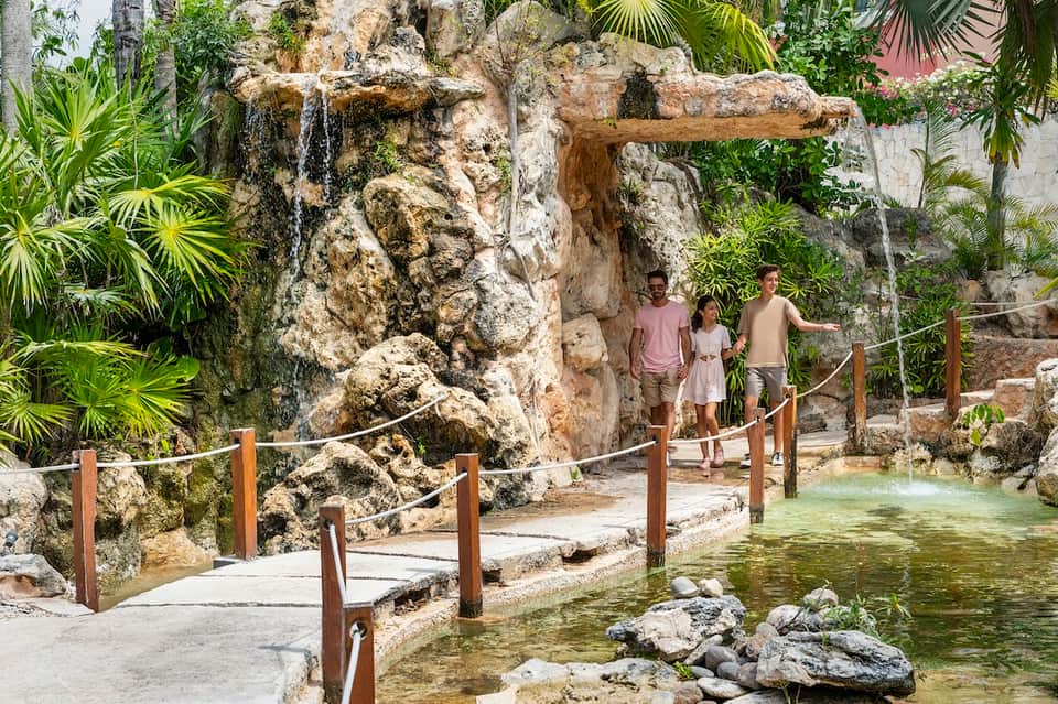 Natural spring cenote with rock formations, tropical vegetation, and visitors enjoying the geological landmark