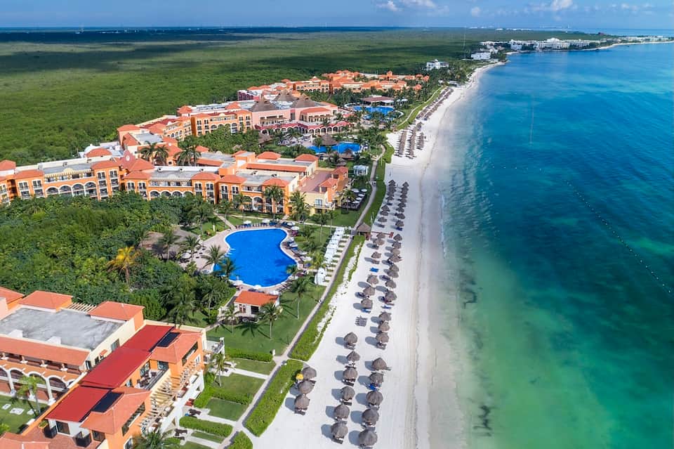 Aerial beachfront resort with pools, manicured grounds, and pristine sandy shoreline