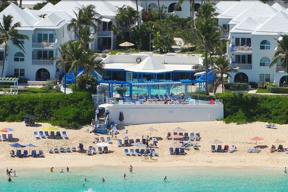 Beachfront resort with white buildings, sandy beach filled with blue lounge chairs, and turquoise ocean