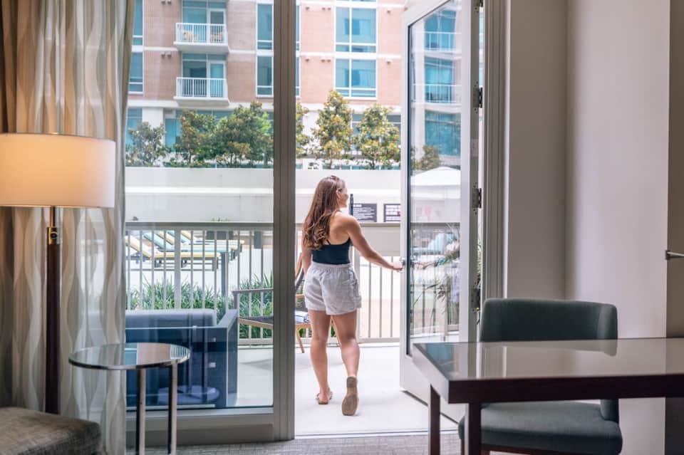 Woman in casual attire standing on hotel balcony overlooking landscaped plaza