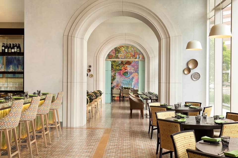Elegant restaurant hallway with arched ceilings, dining tables, bar area, and floral artwork