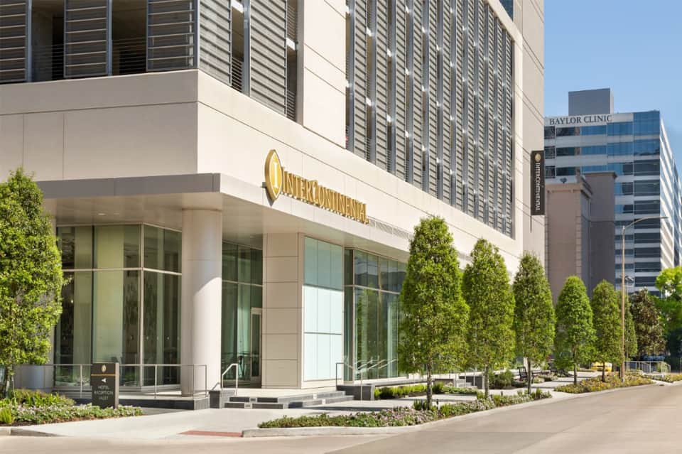 Modern hotel exterior entrance with gold signage, glass doors, and manicured landscaping