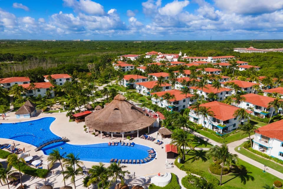 Aerial resort view with blue pools, thatched-roof common areas, and white villas in jungle setting