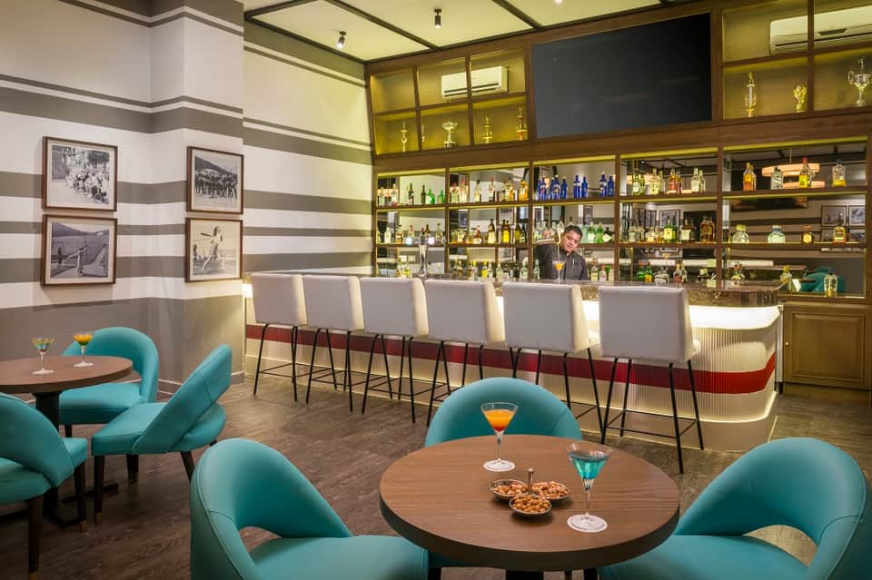 Sophisticated lounge with turquoise mid-century chairs, round tables, and illuminated bar with shelving