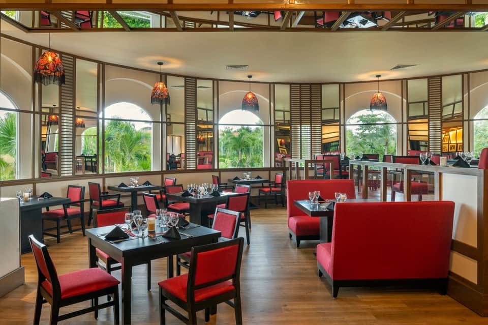 Fine dining restaurant with arched windows, black tables, red chairs, and palm views
