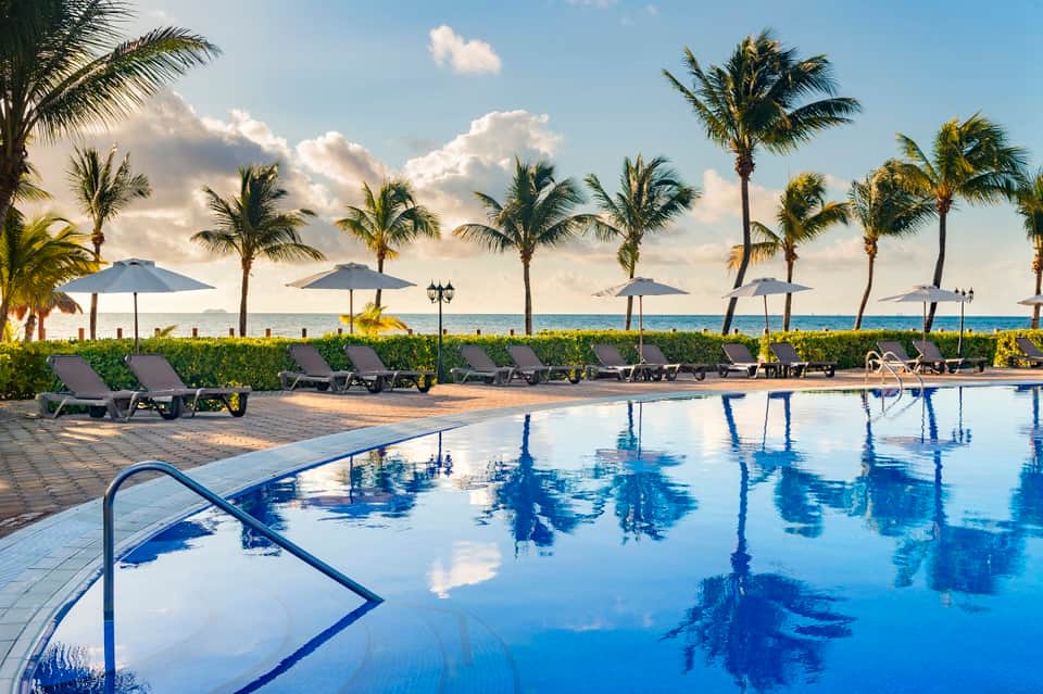 Resort pool with lounge chairs, umbrellas, and palm trees against ocean horizon