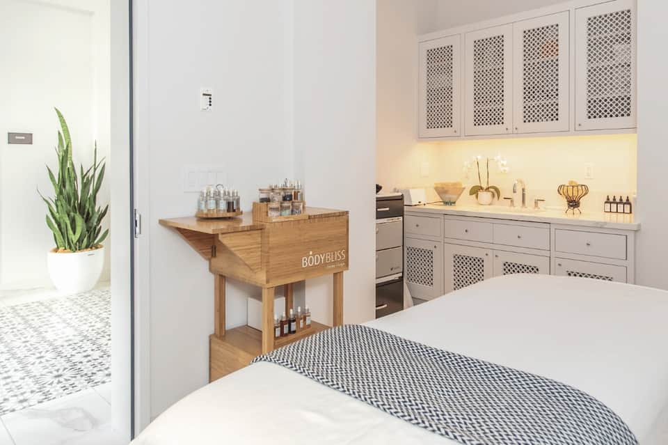 Spa room with massage bed, wooden treatment cart, and cream cabinetry with accent lighting