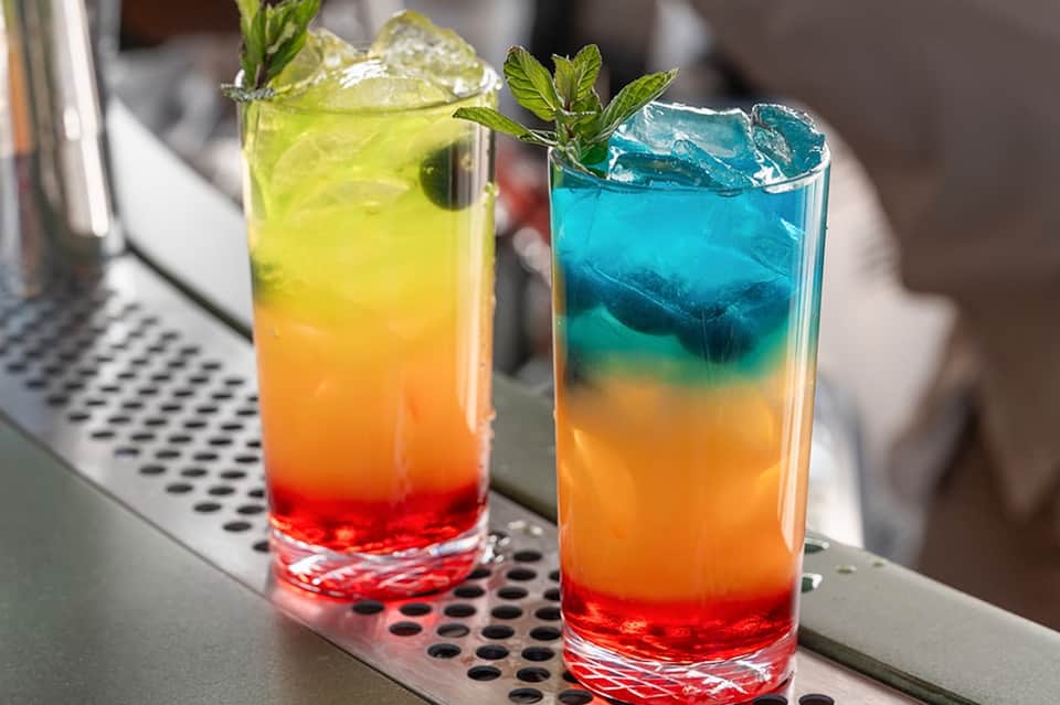 Two colorful layered cocktails with mint garnish on bar counter with blur background