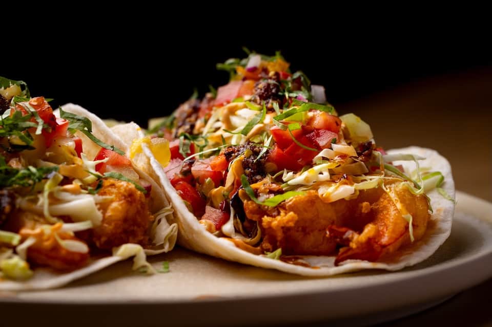 Gourmet fried shrimp tacos with fresh toppings and colorful garnish on white plate