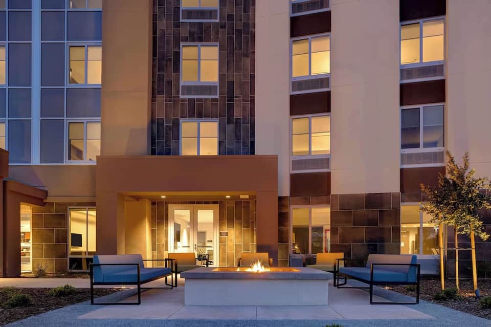 Modern hotel courtyard with firepit, blue lounge chairs, and illuminated building facade