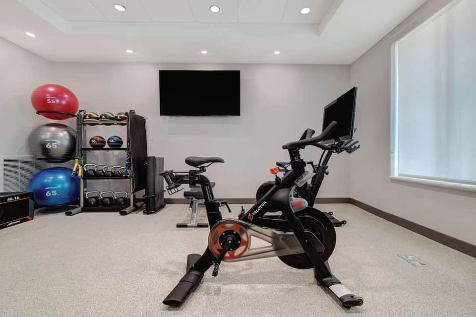 Hotel fitness center with exercise bike, stability balls, free weights, TV screen, and modern equipment rack