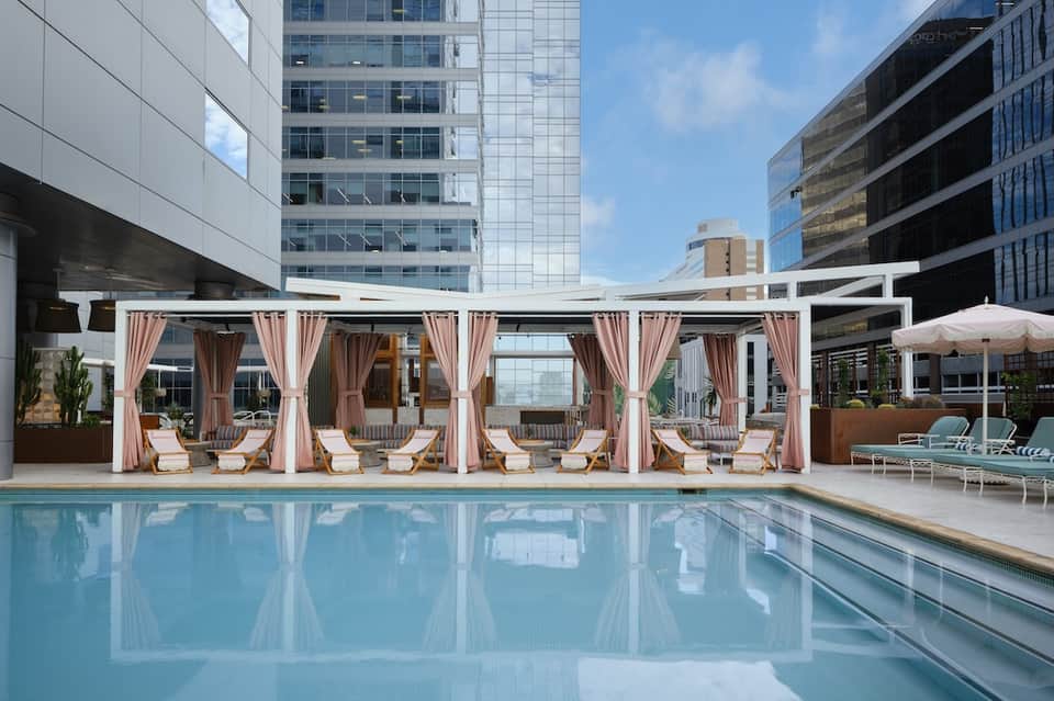 Luxury rooftop pool with pink and white cabanas overlooking city buildings and skyline