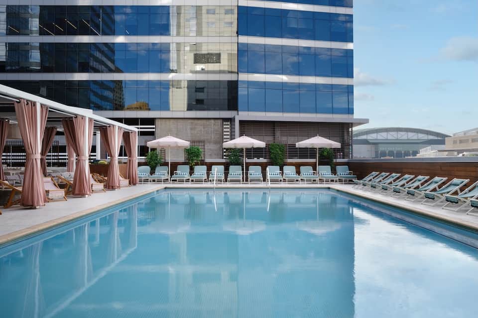 Rooftop infinity pool with city skyline views, pink cabanas, and lounge seating