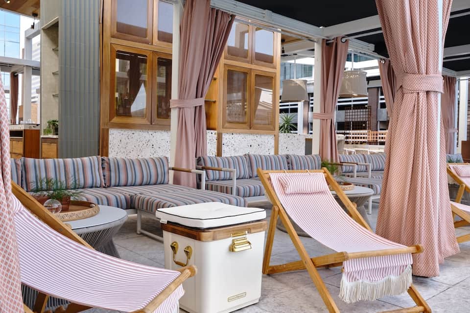 Elegant poolside lounge with striped chaises, wooden furnishings, pink curtains, and seating