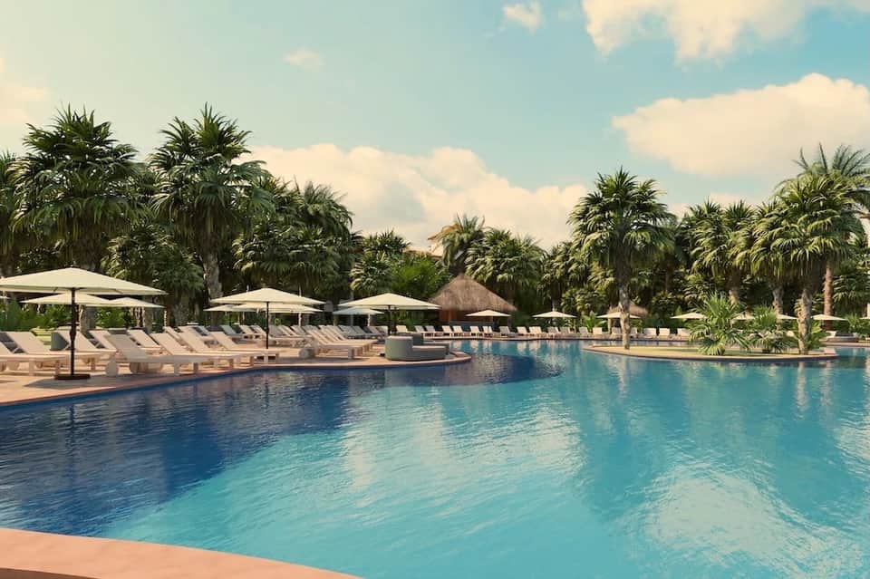 Resort pool surrounded by palm trees, white umbrellas, lounge chairs, and clear blue water
