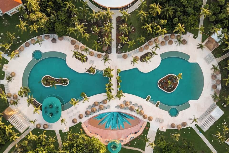Aerial view of resort pools, loungers, landscaping, and tropical grounds in figure-eight pattern
