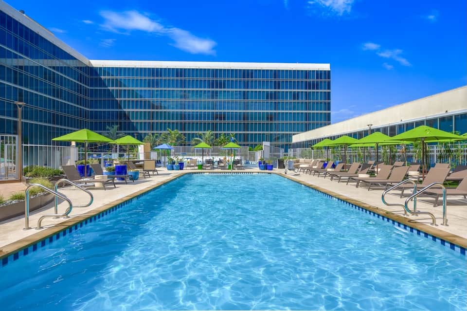 Modern hotel outdoor pool with blue umbrellas, lounge chairs, high-rise building backdrop