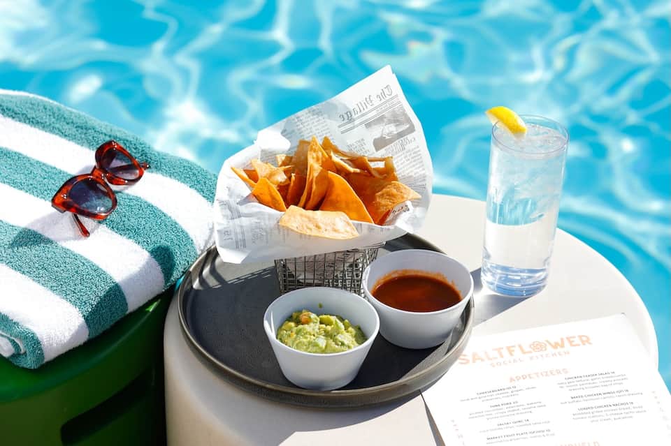 Poolside lunch with French fries, guacamole, water glass, sunglasses, and menu by pool
